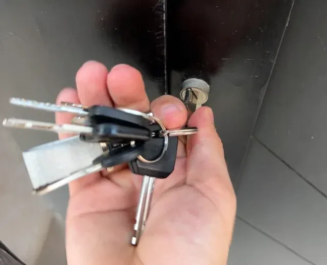 Hand mit Fahrzeugschlüsseln und Schlüsselrohlingen vor einer Fahrzeugtür